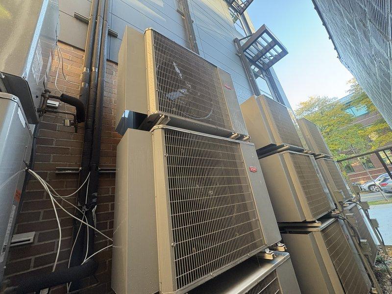 Completed AC tune-up service on exterior-mounted condensing unit and air handler system located on elevated platform against building exterior. Accessed rooftop equipment using extension ladder and performed comprehensive maintenance inspection of multi-unit HVAC installation including refrigerant line checks, electrical connections, and condenser coil assessment.