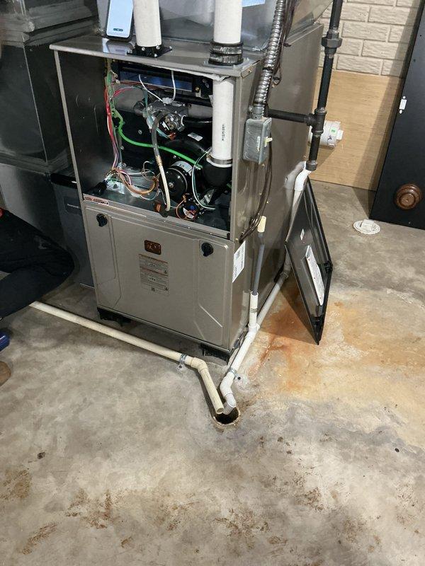 Completed installation of new gas furnace unit in residential basement utility room. Mounted furnace cabinet on concrete floor with proper base support and removed upper access panel to complete internal electrical connections, including wiring of safety controls and motor circuits. Installed dual white PVC vent piping system extending vertically from furnace top through exterior wall for combustion air intake and exhaust venting. 

On building exterior, configured PVC venting termination with multiple elbows to ensure proper clearance and code-compliant discharge positioning. Installed condensate pump assembly with white PVC drain lines connected to furnace condensate outlet and routed to exterior discharge point. Mounted weatherproof electrical disconnect box on exterior wall with appropriate conduit protection for service disconnect requirements.

Verified all electrical connections secure, tested furnace operation, and confirmed proper venting and condensate drainage. Unit left in 
