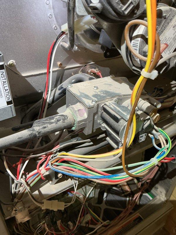 Responded to customer report of smell coming from ductwork. Upon inspection, discovered extensive frost and ice accumulation on evaporator coil assembly and refrigerant lines, indicating system operating in cooling mode or experiencing significant airflow restriction. Inspected gas valve, blower motor housing, and electrical connections on furnace unit, which appeared intact with proper wiring configurations. The heavy frost buildup on upper refrigerant piping and coil surfaces suggests possible thermostat misconfiguration, low refrigerant charge, or restricted airflow causing the coil to freeze and create unusual odors when system cycles. Documented conditions with photographs showing gas valve assembly with multi-colored wire connections and the frozen evaporator coil with ice coating on cylindrical refrigerant line and metal housing components.