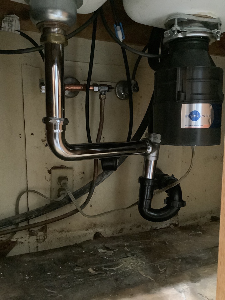 Plumber working on replacement of Kitchen faucet Delta and drains underneath kitchen sink also installing insinkerator garbage disposal 