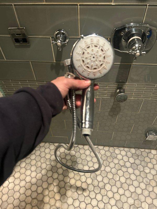 Responded to customer complaint of second-floor shower leak. Inspected detachable showerhead, flexible metal hose, and wall-mounted chrome fixture serving as diverter/mount. Identified and repaired water leakage issue at the connection point of the diverter unit on the tiled wall.