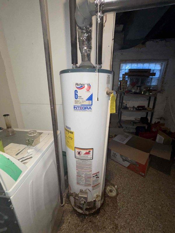 Inspected customer's existing Richmond Integra water heater, which shows active leaking from tank bottom and significant corrosion at base, confirming unit requires replacement. Documented current installation configuration including PVC venting and plumbing connections to facilitate accurate estimate for new water heater installation.