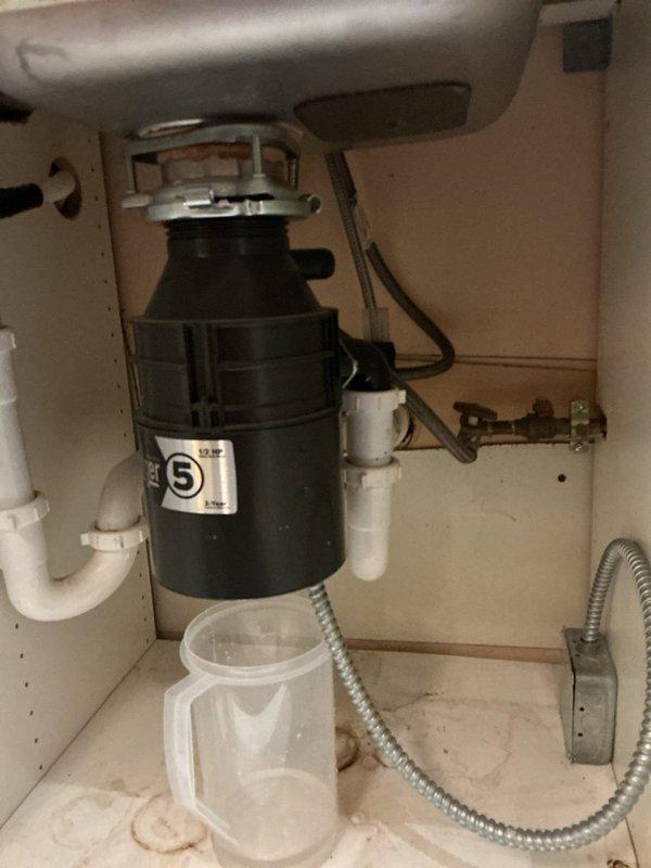 Responded to customer report of leaking garbage disposal and toilet flushing issues. Inspected Badger 5 (1/2 HP) garbage disposal unit under sink which showed signs of previous water leakage. Placed collection container under unit to monitor active leak and performed comprehensive assessment of related plumbing connections including P-trap assembly and drain pipe configuration.