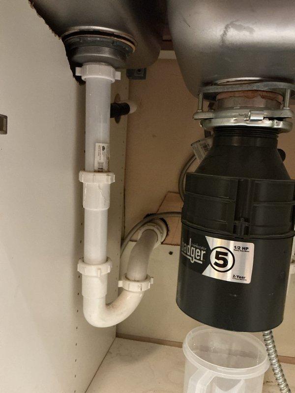 Responded to customer report of leaking garbage disposal and toilet flushing issues. Inspected Badger 5 (1/2 HP) garbage disposal unit under sink which showed signs of previous water leakage. Placed collection container under unit to monitor active leak and performed comprehensive assessment of related plumbing connections including P-trap assembly and drain pipe configuration.
