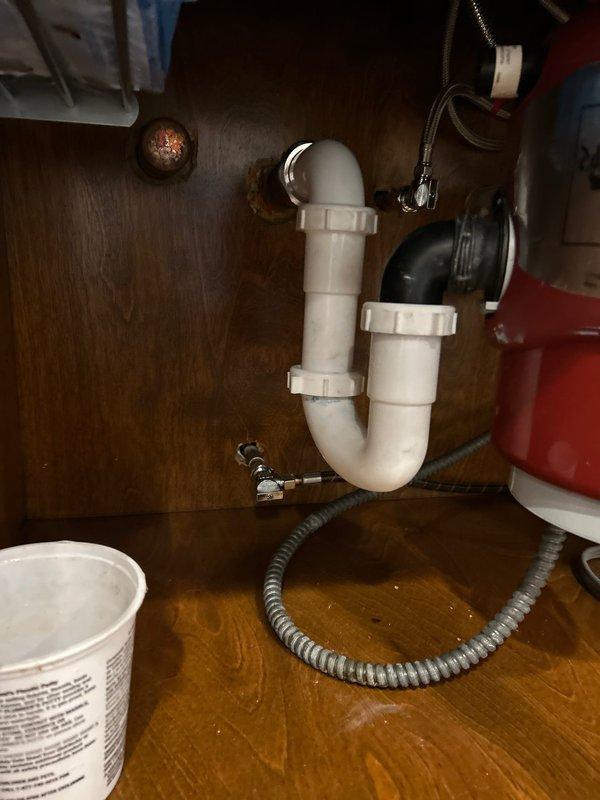Responded to customer report of leaking pipe under kitchen sink. Upon inspection, discovered water accumulation at the connection point between the white PVC P-trap assembly and black drain pipe. Removed existing trap, cleaned pipe threads, and replaced worn gasket causing the leak. Reassembled plumbing connections with appropriate torque and verified complete elimination of leak through extensive testing.