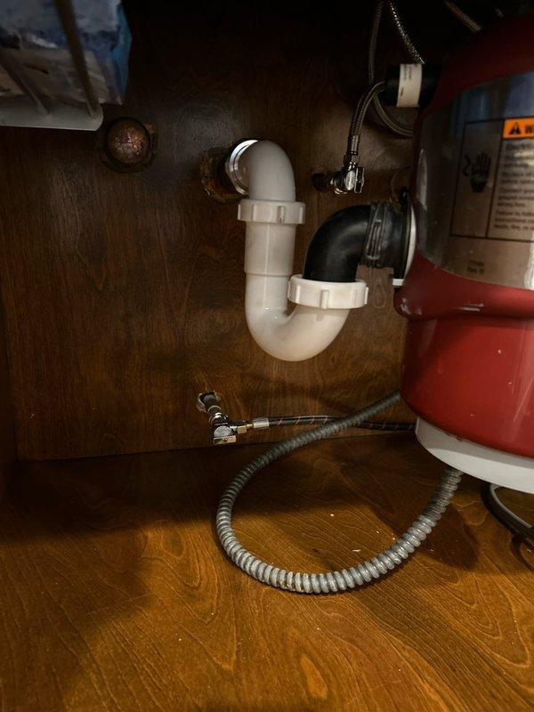 Responded to customer report of leaking pipe under kitchen sink. Upon inspection, discovered water accumulation at the connection point between the white PVC P-trap assembly and black drain pipe. Removed existing trap, cleaned pipe threads, and replaced worn gasket causing the leak. Reassembled plumbing connections with appropriate torque and verified complete elimination of leak through extensive testing.