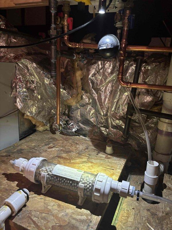 Inspected tankless water heater system after customer reported leak sensor activation. Identified issue with condensate drainage system where water was backing up around condensate output. Observed Condensate Neutralization Capsule was approximately 75% full but not properly draining. Scheduled follow-up appointment to install condensate neutralizer under warranty, noting that hard plastic piping will be required for the condensate drainage due to high attic temperatures.