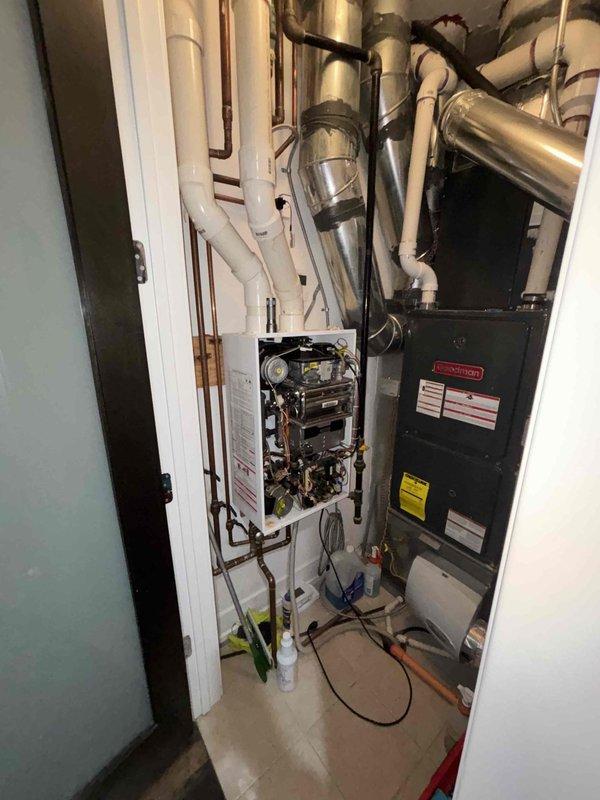 Diagnosed non-operational Novian tankless water heater in utility closet. Visual inspection revealed potential water leak on adjacent PVC pipe with visible rust staining. Accessed internal components of unit through front panel to evaluate control board, valves, and circuitry for proper functionality.