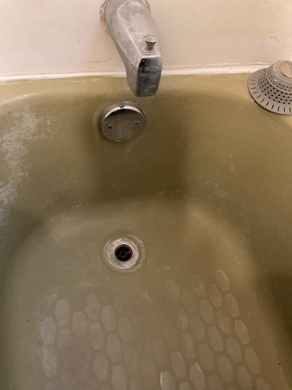 Cleared solid blockage from discolored shower drain in older bathtub. Observed significant mineral buildup and staining throughout the basin. Drain now functioning properly with improved water flow.