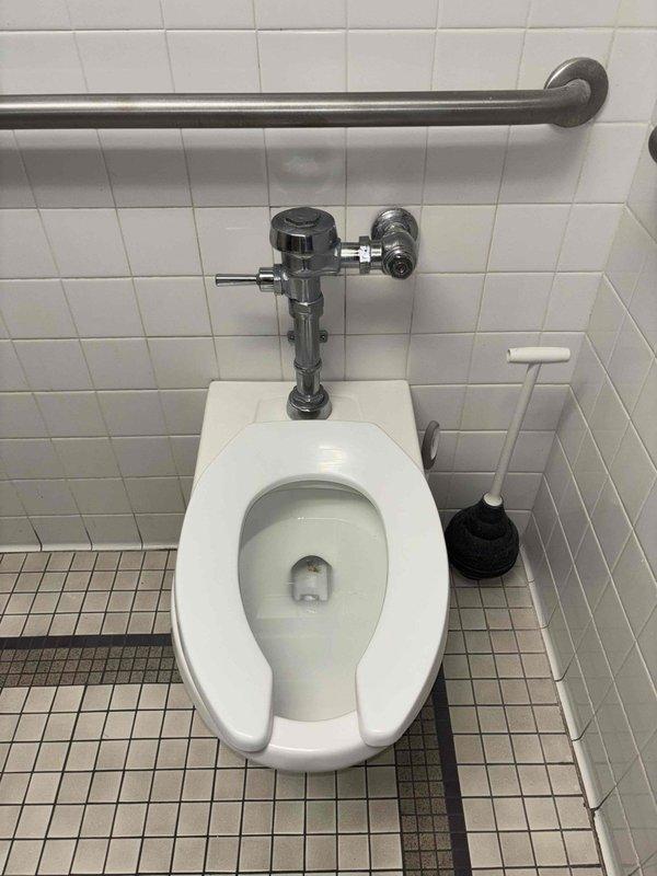 Responded to service call for leaky flush valve on commercial toilet. Inspected wall-mounted toilet with automatic chrome flush mechanism in tile-walled restroom with ADA-compliant grab bar. Repaired flush valve assembly, tested operation, and confirmed proper function with no further leakage.
