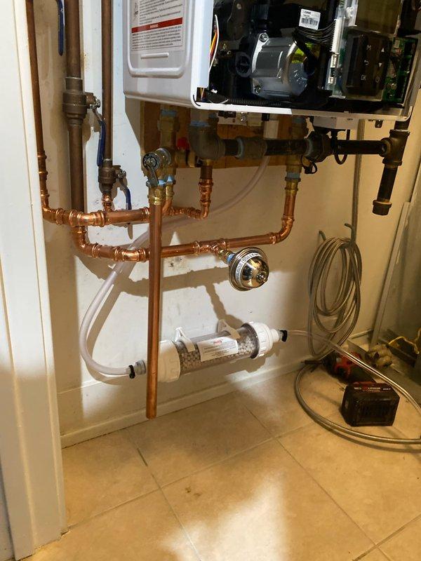 Completed installation of a tankless water heater system with new copper supply lines and a water filtration system with clear housing. Also installed PVC drainage pipes with appropriate elbow joints for washing machine connection, ensuring proper drainage and supply functionality.