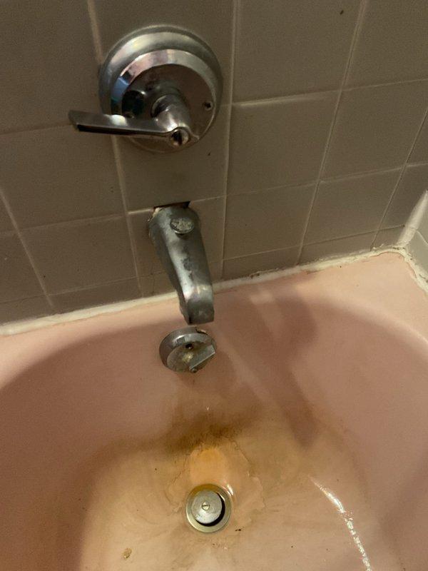 Performed flood control maintenance and inspected Kohler shower/tub fixture with visible leakage. Observed significant mineral buildup and rust staining around the drain area of pink porcelain tub, along with deterioration of chrome spout and handle. Addressed water control issues to prevent further damage to the aging bathroom fixtures.
