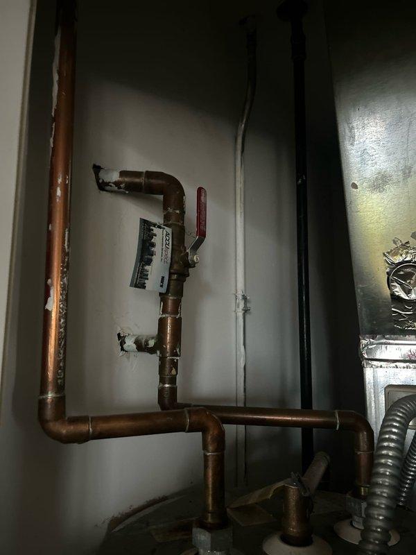 Installed new water shut-off valve behind refrigerator and inspected hot water line configuration. Verified connection integrity of braided supply line to wall access panel. Confirmed proper operation of red-handled shutoff valve on copper piping system.
