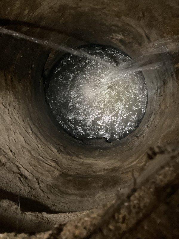 Conducted inspection of sewer system with notable water turbulence and discharge visible in the main line. Documented significant debris accumulation and potential corrosion in the cylindrical drain fixture, with sediment buildup around the central drain opening that could contribute to flooding issues.