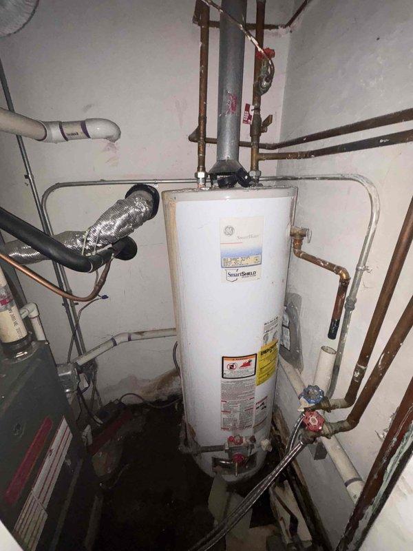 Conducted thorough inspection of 22-year-old GE SmartWater water heater installation, noting significant age-related wear including oxidation and patina formation on copper pipes at connection points. Evaluated current setup featuring copper supply lines, PVC components, and shut-off valves to determine replacement options suitable for the existing confined utility space configuration.
