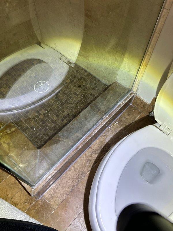 Responded to follow-up service call for water leak diagnosis. Inspected bathroom with reported ceiling damage below. Examination of toilet revealed bowl discoloration and potential seal issues, while shower area showed signs of water intrusion at tile joints and drain connection. Located source of leak at shower drain assembly requiring resealing and toilet flange that needed replacement to prevent further water damage to ceiling below.