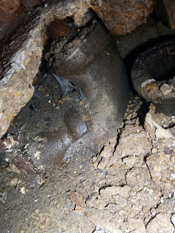 Completed excavation of damaged concrete flooring to access severely corroded main drain line. Exposed circular metal pipe showed significant deterioration with extensive rust and surrounding soil contamination. Replaced deteriorated section with new main line drain pipe after clearing surrounding debris and compromised material.