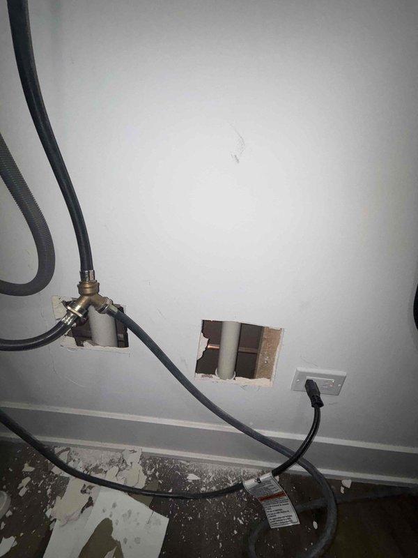 Performed inspection for potential laundry sink drain line installation. Examined existing plumbing access point in wall showing vertical PVC drain pipe with horizontal copper supply lines. Evaluated requirements for proper hook-up and identified necessary modifications to connect new laundry sink to existing plumbing infrastructure.
