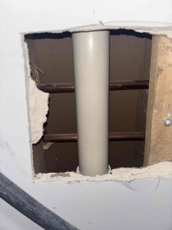 Performed inspection for potential laundry sink drain line installation. Examined existing plumbing access point in wall showing vertical PVC drain pipe with horizontal copper supply lines. Evaluated requirements for proper hook-up and identified necessary modifications to connect new laundry sink to existing plumbing infrastructure.