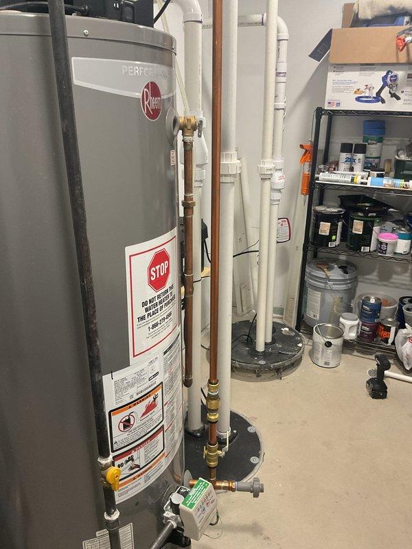 Conducted inspection of reported knocking copper water lines in utility room containing Rheem "Perfection" water heater system. Examined extensive copper pipe network with brass fittings/valves, noting presence of blue pump/motor component mounted on copper piping. Provided customer with replacement and repair options to address noise issue while evaluating potential causes of pipe knocking.