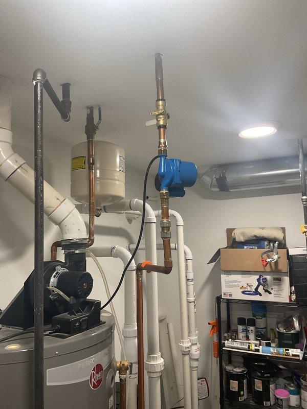 Conducted inspection of reported knocking copper water lines in utility room containing Rheem "Perfection" water heater system. Examined extensive copper pipe network with brass fittings/valves, noting presence of blue pump/motor component mounted on copper piping. Provided customer with replacement and repair options to address noise issue while evaluating potential causes of pipe knocking.
