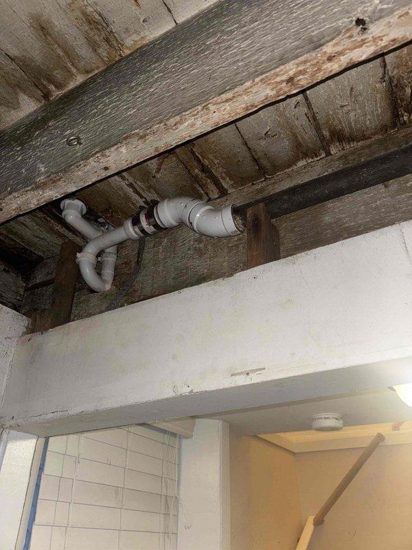 Responded to callback for customer Basi at request of Kevin. Inspected water heater installation in basement utility area, noting proper copper pipe connections and valve placement. Examined ceiling PVC drainage system, identifying signs of previous water damage on surrounding wooden joists and planks. Documented installation conditions with photos for service record.