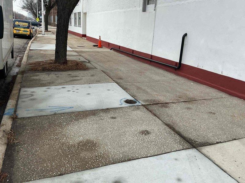 Conducted inspection of aging metal plumbing infrastructure in basement area, documenting significant oxidation and rust formation on pipe surfaces. Identified multiple connection points requiring maintenance, including T-junction and control valve. External inspection of sidewalk area completed with documentation of utility access point and building connection where vertical service pipe enters structure.