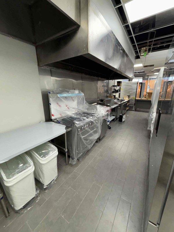 Conducted site evaluation for new restaurant installation requirements. Assessed location for hand wash sink (15"×17") installation and documented existing bathroom fixture conditions. Examined commercial kitchen space for gas line connections needed for range, fryer, and flat top equipment, noting current construction status with installed exhaust hood and protective coverings on kitchen equipment.