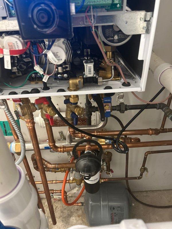 Completed installation of a tankless water heater system with comprehensive copper pipe network. Installed multiple control valves (including red and blue handles), pressure gauge, and black Nav-branded filtration system. Connected all necessary components with proper brass fittings and verified system functionality post-installation.