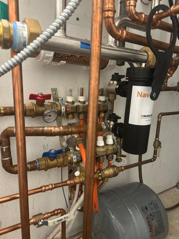 Completed installation of a tankless water heater system with comprehensive copper pipe network. Installed multiple control valves (including red and blue handles), pressure gauge, and black Nav-branded filtration system. Connected all necessary components with proper brass fittings and verified system functionality post-installation.