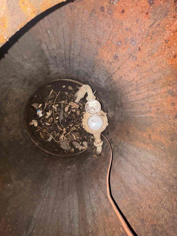 Performed diagnostic assessment of a water main line with active leak reported by customer. Inspection revealed significant corrosion and oxidation on interior pipe walls with visible rust buildup. Located leak source at connection point near water meter assembly. Observed debris accumulation (twigs, leaves) around the meter pit area that required clearing for proper access. System includes copper pipe components and requires yellow insulated pipe section replacement where damage was identified.