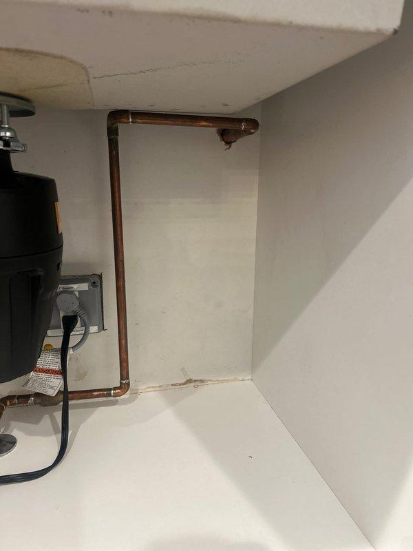 Inspected residential plumbing system for reported burst pipe. Examination revealed corrosion on copper pipes under kitchen sink with visible water damage to cabinet. Also inspected water meter assembly and associated valves in utility closet. Customer had already shut off water under kitchen sink to prevent leakage from external faucet when turned on.