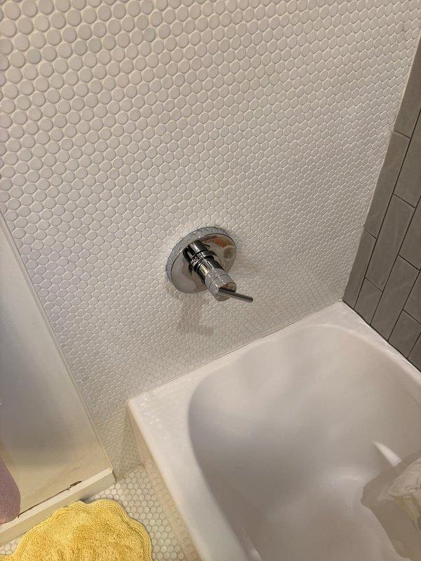Responded to priority service call regarding bathtub leakage from base and through wall. Upon inspection of the modern bathroom with dual-tile design (subway pattern and hexagonal mosaic), identified faulty shower valve control fixture causing water penetration behind walls. Repaired valve assembly and sealed connection points to prevent further leakage.