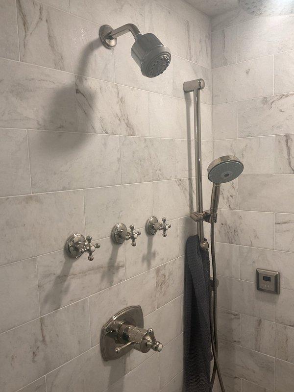 Conducted comprehensive assessment of customer's existing shower system for potential replacement. Evaluated current installation featuring dual shower heads (ceiling-mounted rainfall and wall-mounted handheld), brushed nickel fixtures, and marble-effect tile surround. Noted some water staining/discoloration on ceiling tiles that may indicate underlying issues requiring attention during replacement.
