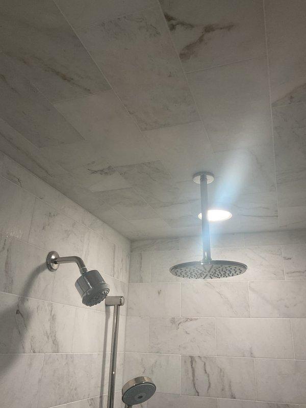 Conducted comprehensive assessment of customer's existing shower system for potential replacement. Evaluated current installation featuring dual shower heads (ceiling-mounted rainfall and wall-mounted handheld), brushed nickel fixtures, and marble-effect tile surround. Noted some water staining/discoloration on ceiling tiles that may indicate underlying issues requiring attention during replacement.