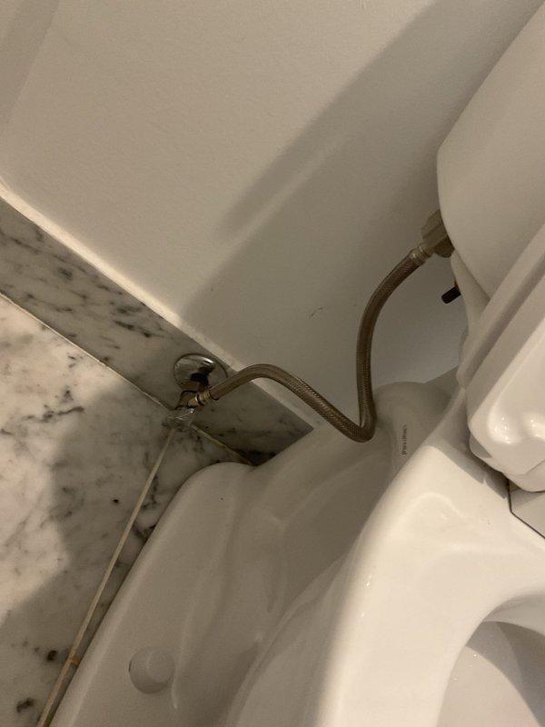 Responded to emergency service call for overflowing toilet. Inspected plumbing connections including supply line and wall valve. Removed tank lid to examine internal components, noting a green float ball mechanism and some mineral buildup around the drain assembly. Corrected overflow issue and restored proper toilet function.