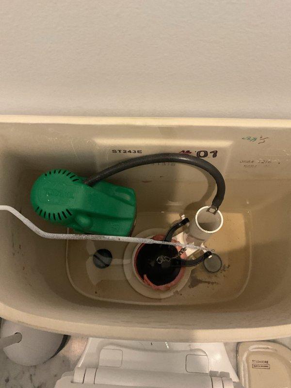 Responded to emergency service call for overflowing toilet. Inspected plumbing connections including supply line and wall valve. Removed tank lid to examine internal components, noting a green float ball mechanism and some mineral buildup around the drain assembly. Corrected overflow issue and restored proper toilet function.