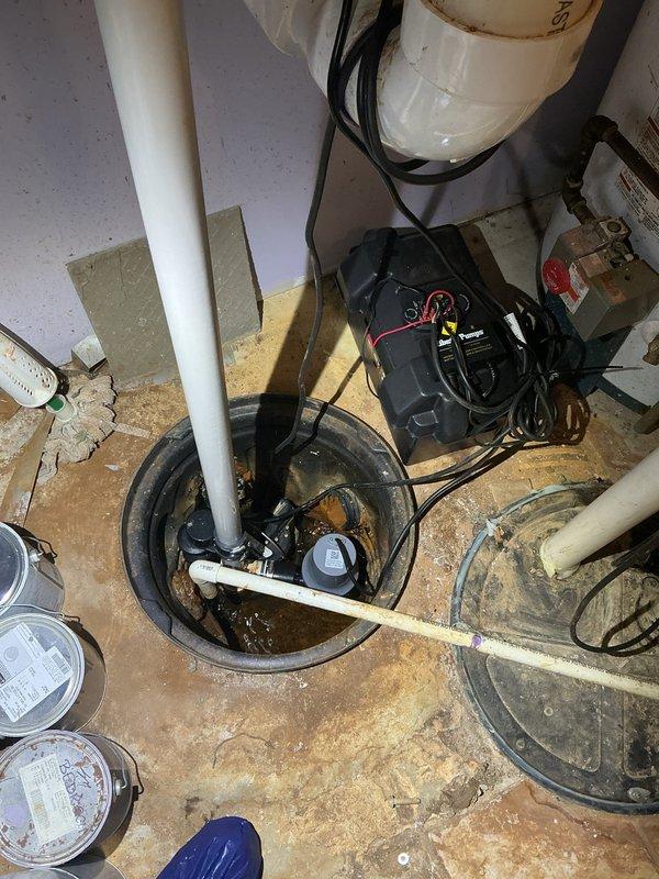 Inspected sump pump system in residential basement after removing carpet access panel. Observed standing water in the sump pit with current pump system and backup power supply in place. Provided estimate for recommended service.