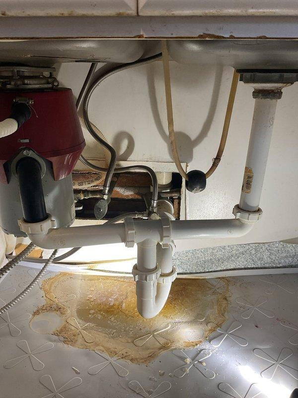 Responded to service call for slow draining tub with reported backup issues when washing machine and sink are used. Inspection revealed significant plumbing issues including a leaking P-trap under the kitchen sink with visible water damage to the cabinet floor and extensive rust corrosion along the sink edges. Recommended replacement of damaged P-trap assembly and sink due to deterioration, along with installation of new garbage disposal as requested.