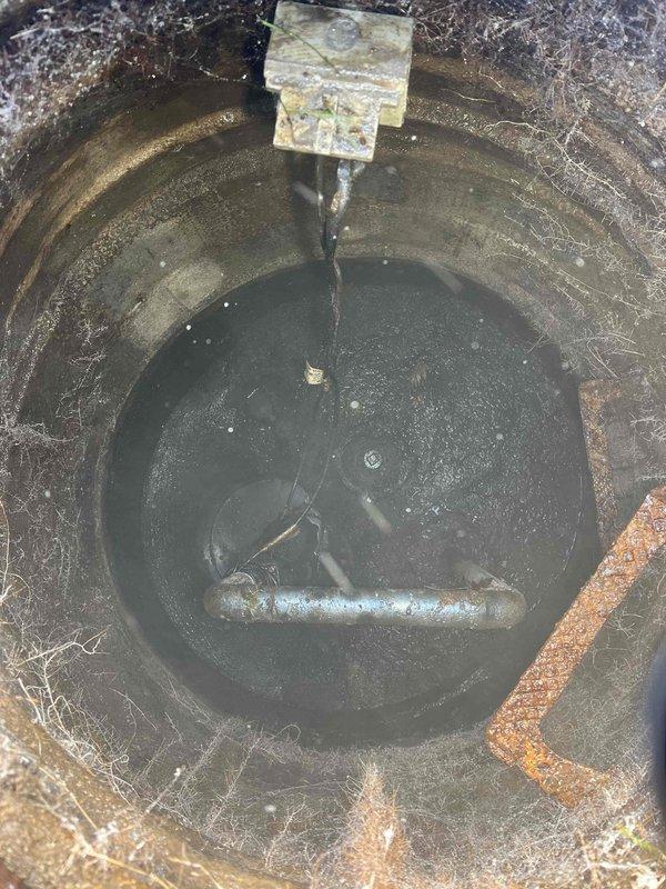 Responded to a service call for a drainage issue. Inspected a drainage pit containing stagnant water with significant mineral buildup, algae growth, and corrosion on metal components. Identified and accessed the exterior cleanout cap located in snow-covered ground to prepare for the scheduled repair work.