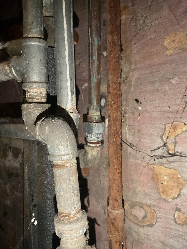 Performed diagnostic assessment on a leaking 50-gallon natural gas water heater approximately 20 years old. Inspection revealed significant corrosion at pipe connections and visible water damage to surrounding wooden structures. Observed rust formation on galvanized steel pipes, particularly at joint connections, indicating progressive deterioration. Recommended replacement of the aging unit due to its condition and exceeded service life expectancy.