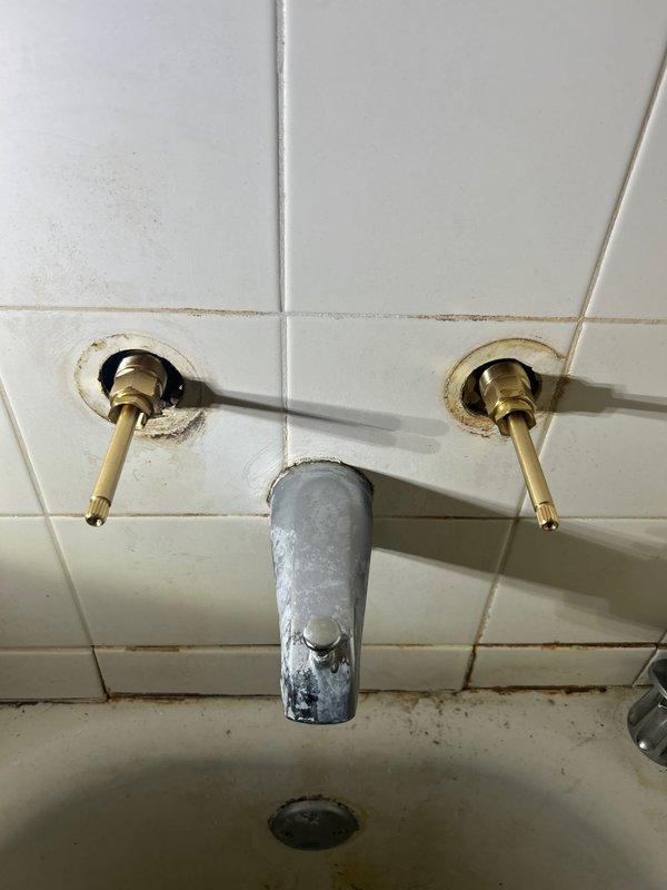 Completed replacement of deteriorated bathroom sink faucet assembly. Removed existing chrome handles and central spout which showed significant calcium/mineral buildup and wear. Installed new fixture set, ensuring proper sealing at wall tile connections to prevent water damage and mildew formation around valve openings.