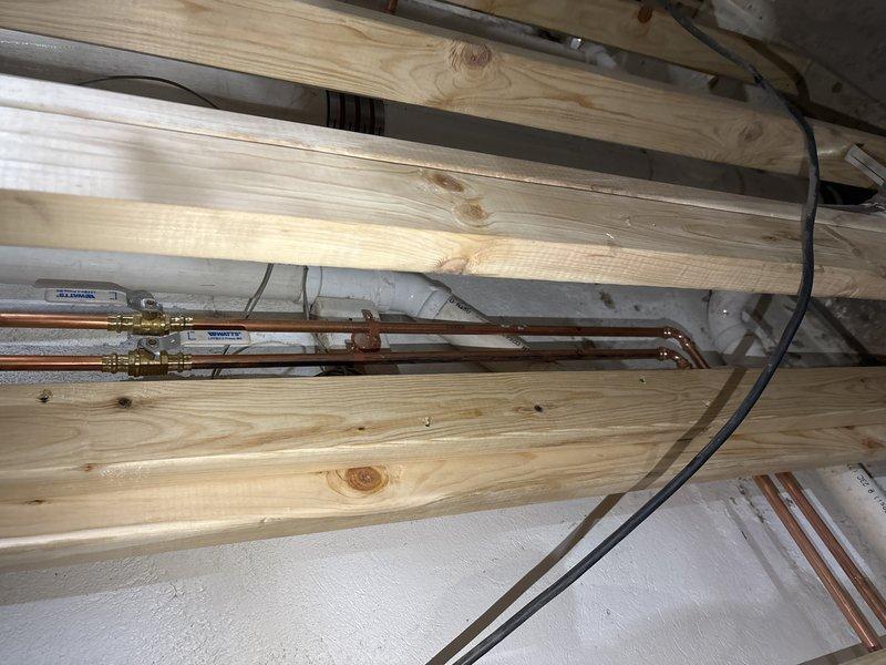 Performed callback inspection of copper supply lines and gas piping in basement utility area. Examined window framing with exposed plumbing infrastructure and evaluated condition of copper pipes running between floor joists. Documented installation with photos for further assessment as requested by Chris L.