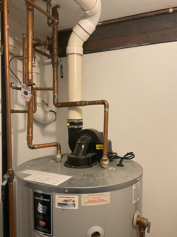 Performed assessment of existing residential water heater system for potential replacement. Current unit is aging with standard tank design featuring copper supply lines, circulator pump, and PVC venting system. Customer is interested in converting to a tankless water heater solution. Documented current installation configuration to prepare detailed conversion estimate.