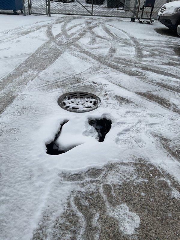 Conducted site inspection of reported sinkhole adjacent to manhole in snow-covered paved area. Visual assessment revealed potential undermining of pavement around drainage structure, with multiple depressions indicating possible pipe failure or soil erosion beneath surface. Recommended camera inspection to evaluate pipe integrity and determine extent of underground damage prior to excavation, repair/replacement of affected pipe sections, and backfilling to restore surface stability.