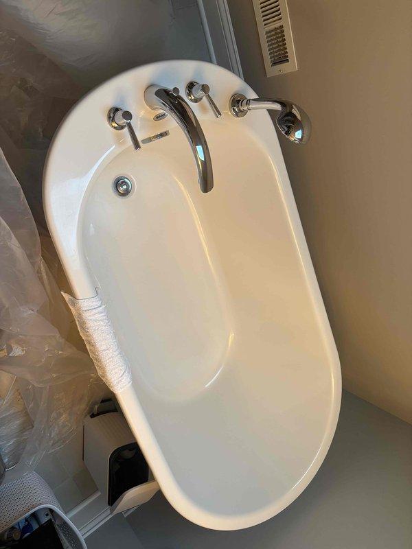 Completed installation of a new white oval bathtub with chrome fixtures including curved faucet spout and separate hot/cold handles. Assessed client's request to replace shower head and fixtures while converting existing double vanity to single vanity configuration.