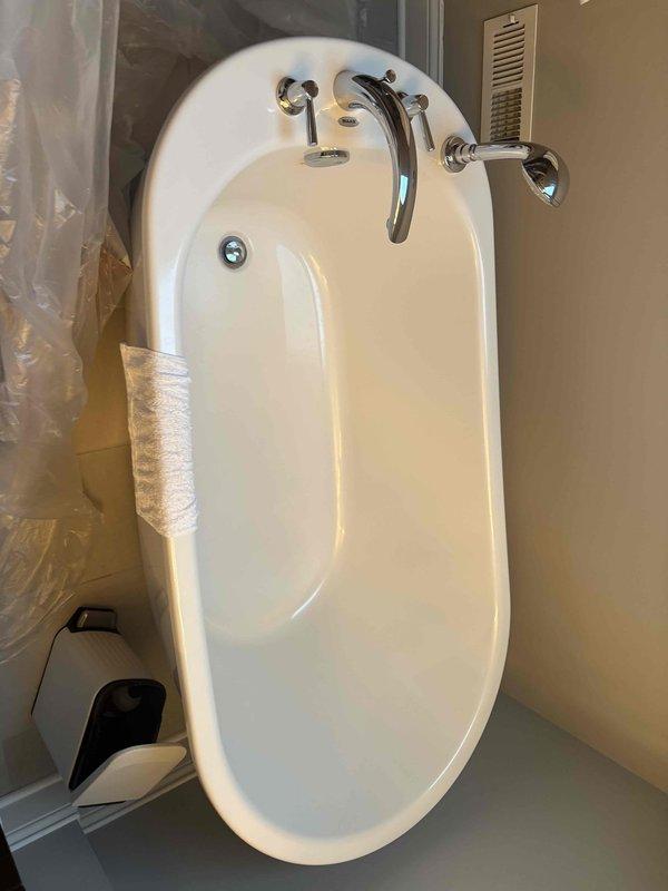 Completed installation of a new white oval bathtub with chrome fixtures including curved faucet spout and separate hot/cold handles. Assessed client's request to replace shower head and fixtures while converting existing double vanity to single vanity configuration.