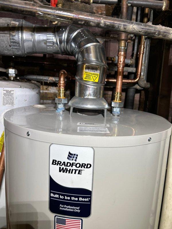 Successfully installed a Bradford White tanked water heater in utility area with proper venting and copper pipe connections. Installation included necessary valves and fittings while adhering to the 56" height restriction requirement by using a standard/low profile model rather than slim design. All components were properly secured with no leaks observed during final inspection.