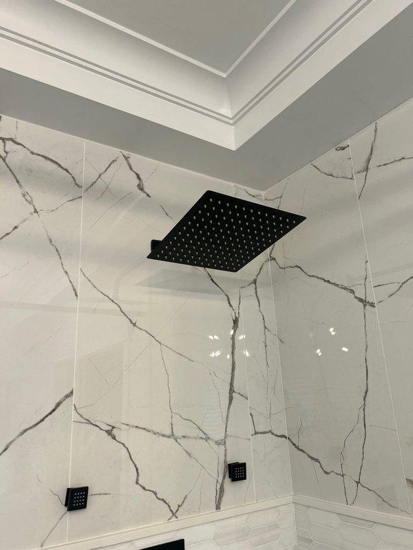 Installed new modern black thermostatic shower valve with dual hot and cold controls on white tiled wall. System includes a ceiling-mounted square black rainfall showerhead with multiple water distribution points, completing the contemporary bathroom fixture upgrade as sold by Jacob.
