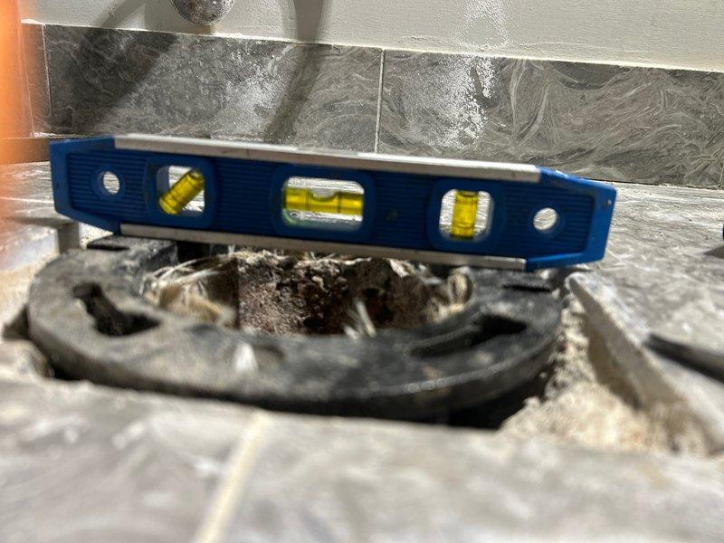 Inspected toilet drainage system and confirmed issue with unlevel flange and pipe causing persistent seal failures. Verified with spirit level that existing flange installation had significant pitch, leading to loose bolts and failed wax seals. Removed toilet, replaced damaged flange assembly and corrected pipe alignment to ensure proper drainage angle and secure mounting surface.